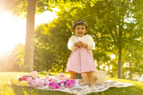 Niña sonriente de pie sobre una manta en un parque, iluminada a contraluz por la luz del atardecer.